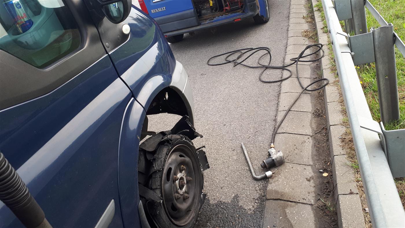 Rozerwana opona auta dostawczego przy barierce, obok sprzęt i bus Mobile Gum